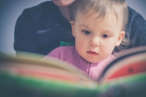 Jeune enfant regardant un livre accompagné par un adulte
