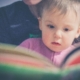 Jeune enfant regardant un livre accompagné par un adulte
