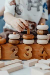 jeune enfant manipulant des anneaux en bois lors d’une activité d’éveil accompagné de professionnels petit enfance